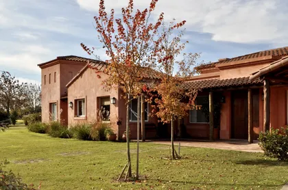 Casa terracota con galería cubierta y árbol joven en jardín verde — proyecto San Francisco 1, por Marconi Silva Arquitectos, en Manzanares