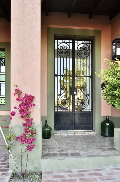 Entrada de casa con puerta de hierro forjado y plantas enredaderas — proyecto Valle Claro, por Marconi Silva Arquitectos, en Benavidez