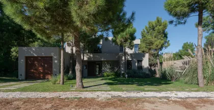 fachada moderna de hormigón con pinos y amplias ventanas — proyecto Costa Esmeralda 1, por Arquitecto Caceres, en Costa Esmeralda
