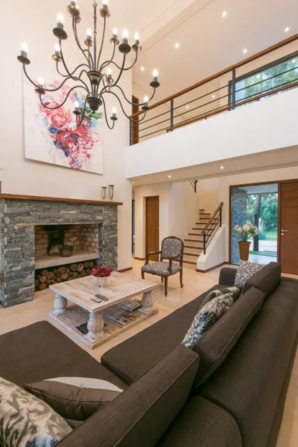 Living amplio de doble altura con chimenea y araña prominente — proyecto Costa Esmeralda 2, por Arquitecto Caceres, en Costa Esmeralda