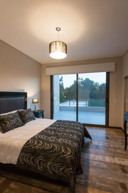 Dormitorio moderno con cama king, ventanales y luz cálida — proyecto Costa Esmeralda 2, por Arquitecto Caceres, en Costa Esmeralda