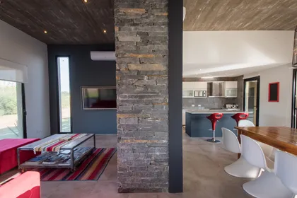 Living moderno con isla de cocina y paredes de piedra — proyecto Costa Esmeralda 3, por Arquitecto Caceres, en Costa Esmeralda