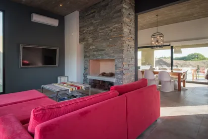 Living moderno con hogar de piedra y sillón rojo — proyecto Costa Esmeralda 3, por Arquitecto Caceres, en Costa Esmeralda