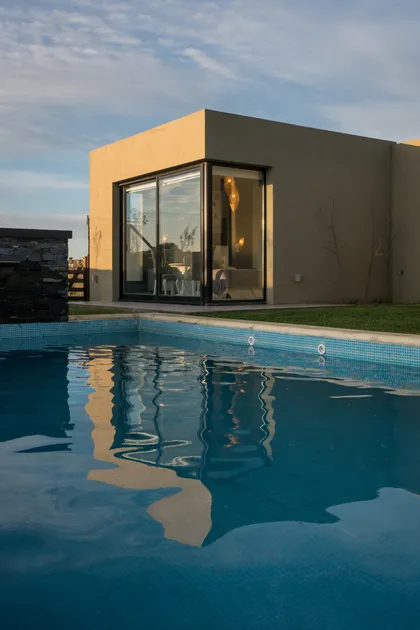 Piscina moderna con reflejos y casa minimalista — proyecto Costa Esmeralda 3, por Arquitecto Caceres, en Costa Esmeralda