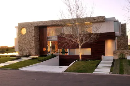 Fachada moderna con piedra, madera y grandes ventanales — proyecto Casa Cardales, por Barrionuevo Arquitects, en Los Cardales