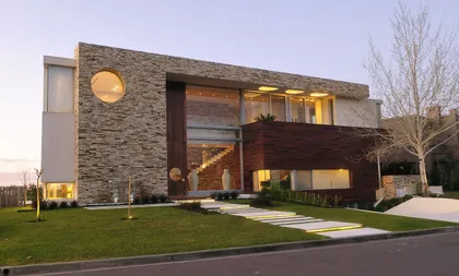 Casa moderna con fachada de piedra y madera y ventana circular — proyecto Casa Cardales, por Barrionuevo Arquitects, en Los Cardales