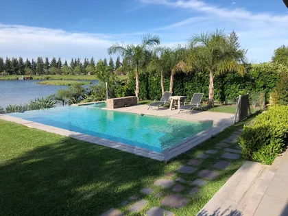Piscina infinita moderna con deck de madera y vegetación exuberante — proyecto Santa Barbara, por Estudio Moreto Bensusan, en Benavidez