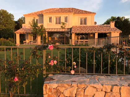 Fachada mediterránea con jardín de rosas y luz de atardecer — proyecto Pilará, por Estudio Moreto Bensusan, en Pilar