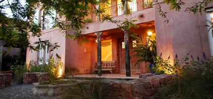 Fachada rústica mediterránea con vegetación exuberante e iluminación cálida — proyecto Laguna del Sol, por Estudio Moreto Bensusan, en Tigre