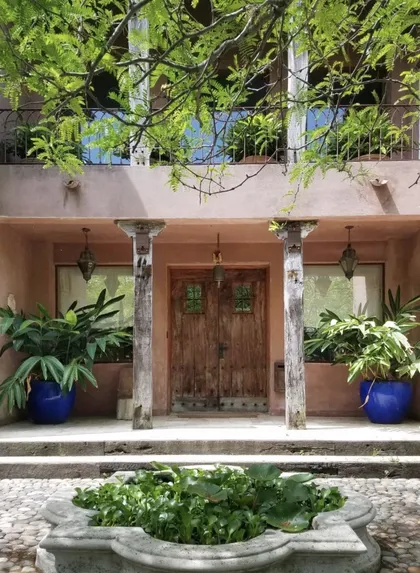 Fachada mediterránea con puertas de madera rústica y vegetación exuberante — proyecto Laguna del Sol, por Estudio Moreto Bensusan, en Tigre