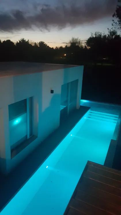 Piscina moderna de noche con escalones integrados e iluminación azul — proyecto Los Ceibos, por Cuello Selva, en Tigre
