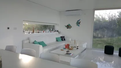 Living moderno minimalista con sofá blanco y grandes ventanales — proyecto Costa Esmeralda, por Cuello Selva, en Costa Esmeralda