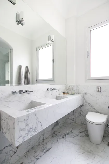 Baño moderno luminoso con doble bacha de mármol blanco y grifería de pared — proyecto Libertador y Salguero, por Estudio Magrane, en CABA