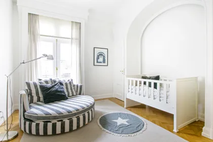 Dormitorio de bebé moderno con cuna y banco rayado, piso de madera — proyecto Libertador y Salguero, por Estudio Magrane, en CABA