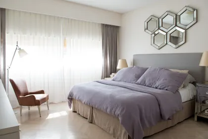 dormitorio moderno con cama grande y sillón tapizado beige — proyecto San Martín de Tours, por Estudio Magrane, en CABA