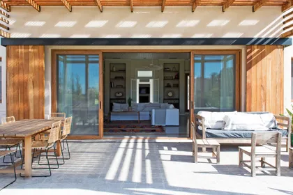 Galería exterior con mesa de madera y living integrado, vistas al jardín — proyecto Santa María de Lobos, por Estudio Magrane, en Lobos