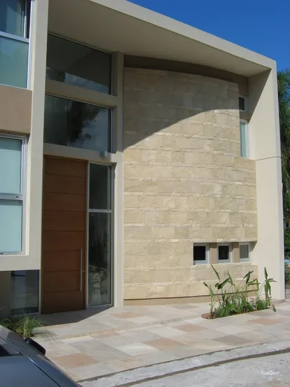 Fachada moderna con puerta de madera grande y revestimiento de piedra — proyecto Casa en San Isidro, por GEN STUDIO COMOTTO - SOMMER , en San Isidro