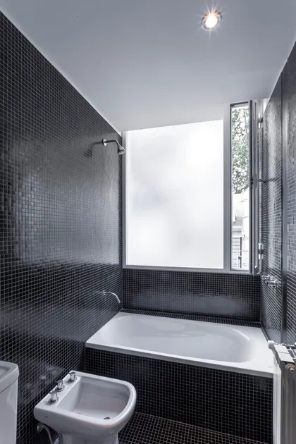 Baño moderno con azulejos negros y bañera exenta — proyecto PH Tamborini , por ariana werber arquitecta, en Núñez
