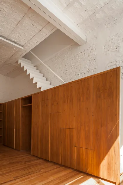 Habitación moderna con amplios armarios de madera y escalera flotante — proyecto PH Tamborini , por ariana werber arquitecta, en Núñez
