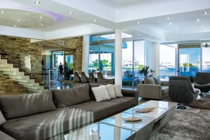 Living moderno con ventanales y detalles en piedra y madera — proyecto La Reserva Cardales I, por ARQCONS, en Los Cardales