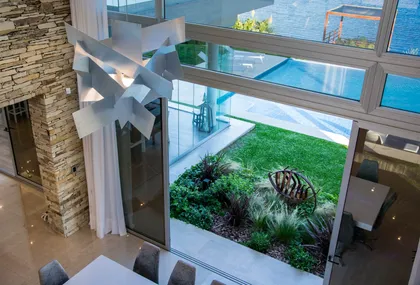 Living moderno con ventanales, piedra y jardín exterior — proyecto La Reserva Cardales I, por ARQCONS, en Los Cardales