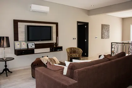 Sala de estar moderna con sofá marrón en forma de U y sillón de ratán — proyecto Casa Reserva Cardales II, por ARQCONS, en Los Cardales