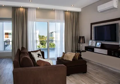 Living moderno con ventanas amplias y sofá marrón — proyecto Casa Reserva Cardales II, por ARQCONS, en Los Cardales