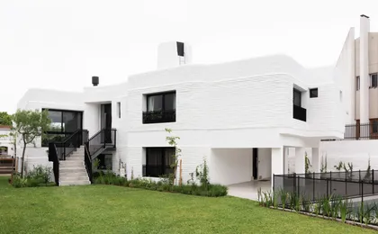 Fachada de casa moderna blanca con ladrillo texturizado y grandes ventanales — proyecto Boating I, por Estudio Arq. Ana M. Carrera, en Boating Club