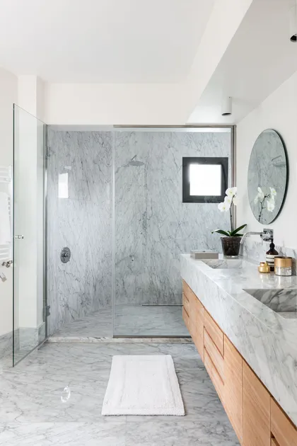 Baño moderno con mármol gris, vanitory flotante de madera y ducha vidriada — proyecto Boating I, por Estudio Arq. Ana M. Carrera, en Boating Club