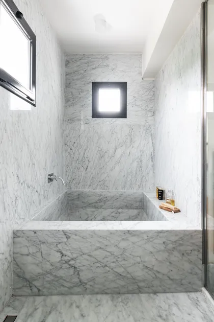 Baño minimalista de mármol blanco con bañera integrada y luz natural — proyecto Boating I, por Estudio Arq. Ana M. Carrera, en Boating Club