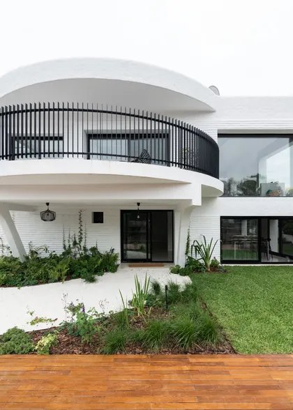 Fachada moderna blanca con balcón curvo y jardín exuberante — proyecto Boating I, por Estudio Arq. Ana M. Carrera, en Boating Club