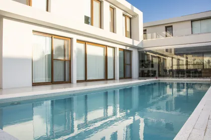 Amplia piscina moderna junto a fachada blanca y cristal — proyecto CASA GOLF, por Ramirez Arquitectura, en Nordelta