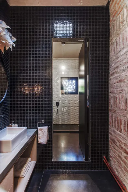 Baño moderno industrial con mosaicos negros y ladrillo expuesto — proyecto Casa Lavalle, por Silvia Soqueff, en CABA