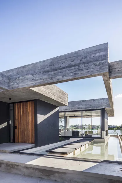 Fachada moderna con pérgola de hormigón y puerta de madera — proyecto Bamboo House, por Estudio PK