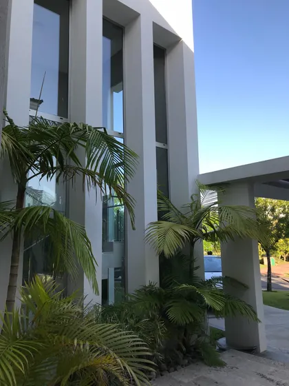Fachada moderna con palmeras y ventanas de piso a techo — proyecto San Isidro Labrador, por GreenArq - Carolina Faverio , en San Isidro