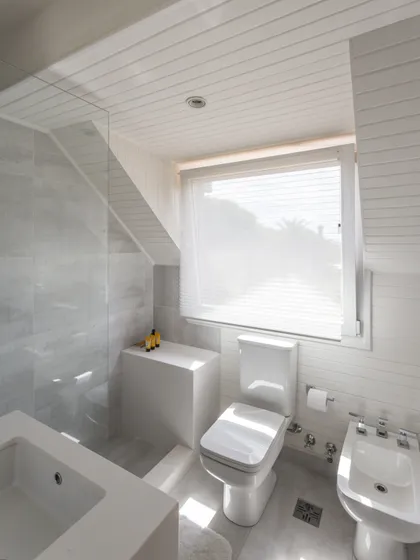 Baño minimalista blanco con bañera, inodoro y ventanal luminoso — proyecto The Classic, por BAS Y GARCIA , en San Isidro