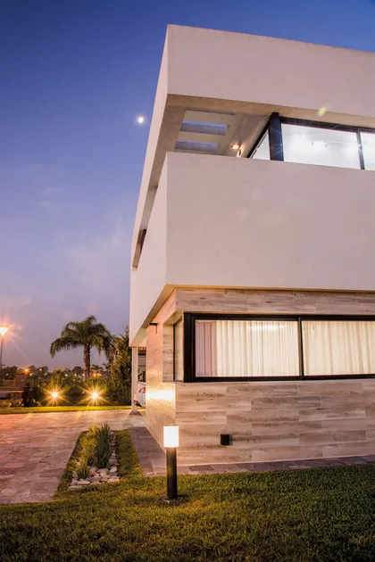 Casa moderna de dos pisos con fachada blanca y revestimiento de madera al atardecer — proyecto CASA V, por DX ARQ