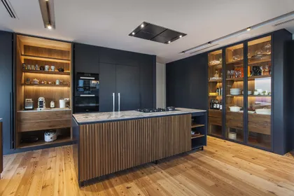 Cocina moderna con isla central, muebles negros y madera clara — proyecto Casa India , por Estudio Simbiosis