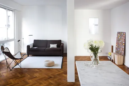 Living minimalista con sofá negro, piso parquet y flores blancas — proyecto Departamento Barrancas, por Ekaterina Kunzel Arquitecta, en Belgrano