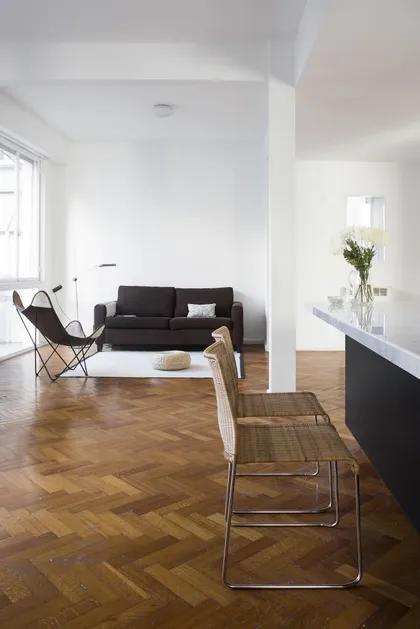 Living minimalista con sofá negro, piso de madera y doble altura — proyecto Departamento Barrancas, por Ekaterina Kunzel Arquitecta, en Belgrano