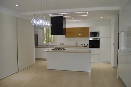 Cocina moderna de planta abierta con isla blanca y luces colgantes — proyecto PINAMAR NORTE, por LADAGA-RUARTE-Pinamar, en Pinamar