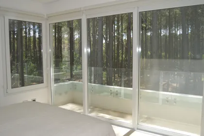 Dormitorio moderno con vista al bosque a través de ventanales — proyecto PINAMAR NORTE, por LADAGA-RUARTE-Pinamar, en Pinamar