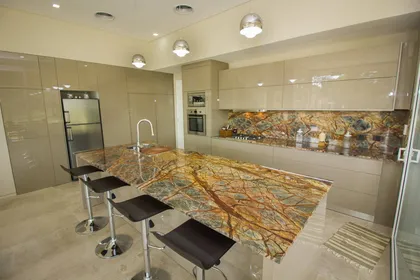 cocina moderna con isla de piedra llamativa y gabinetes brillantes — proyecto LA HERRADURA - Boulevard III, por LADAGA-RUARTE-Pinamar, en Pinamar