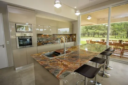 Cocina moderna con isla de piedra espectacular y vistas al bosque — proyecto LA HERRADURA - Boulevard III, por LADAGA-RUARTE-Pinamar, en Pinamar