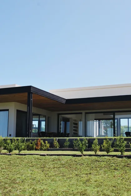 Fachada moderna con amplias ventanas y techo voladizo de madera — proyecto Pilará 38, por Detry Miguens Arquitectura, en Pilará