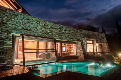 Casa moderna con piscina iluminada y fachada de piedra por la noche — proyecto Casa Villa La Angostura 2, por Sidoni & Asociados, en Villa La Angostura