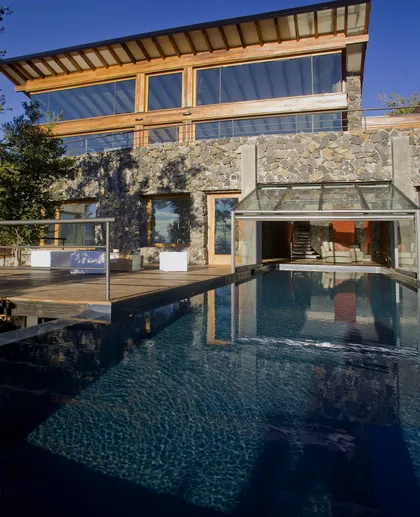 Casa moderna rústica con piscina infinita y fachada de vidrio plegable — proyecto Casa Muelle de Piedra, por Sidoni & Asociados, en Villa La Angostura