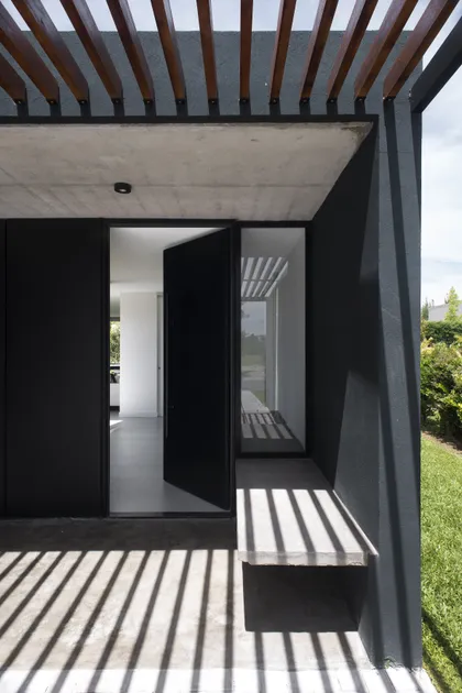 fachada moderna con puerta pivotante negra y pérgola — proyecto Casa 2LH, por Luciano Kruk
