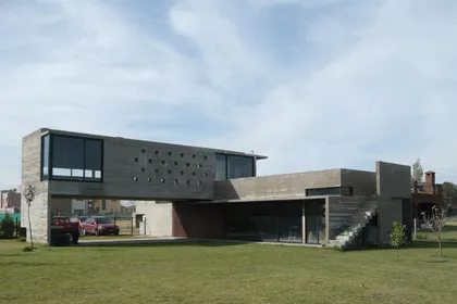 Casa contemporánea con fachada de hormigón y ladrillo, amplio jardín verde — proyecto Casa Canning, por Luciano Kruk, en Canning