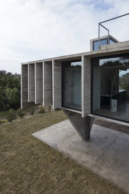 Casa moderna hormigón con grandes ventanales y pérgola lateral — proyecto Casa Cariló, por Luciano Kruk, en Cariló
